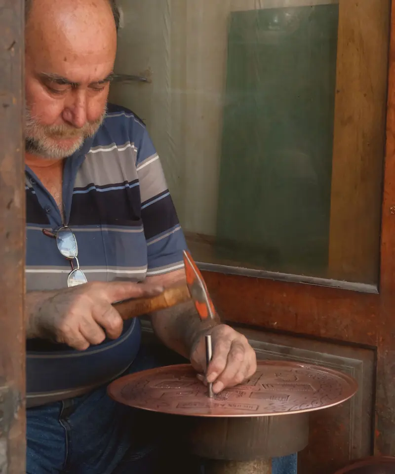 Bakırcının elleri, çekiç ve kalemle bakır tabağı işliyor